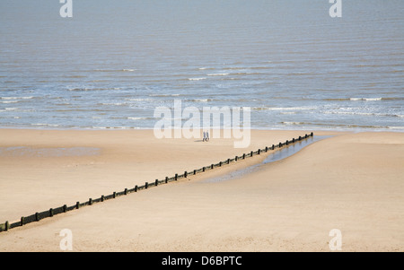 Les gens qui marchent sur une large plage de sable vide à Frinton and on Sea, Essex, Angleterre Banque D'Images