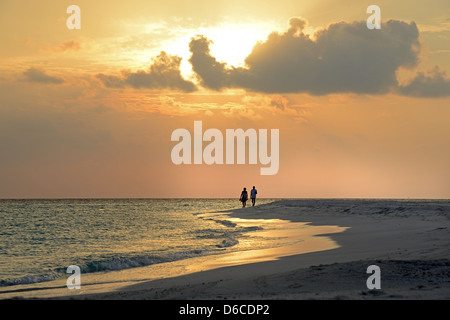 Un couple qui se profile à pied le long d'une plage de sable fin au coucher du soleil sur l'île de Kuramathi sur Alifu Alifu Atoll en Thew aux Maldives. Banque D'Images