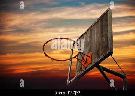 Basket-ball de rue. Ancien panier de basket-ball et un retour conseil dans le coucher du soleil contre le ciel orange foncé. Banque D'Images