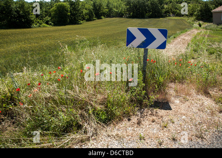 Chevron bleu flêchage pointant à droite indiquant un virage de la route, en France, la voie menant à l'écart à droite.Sunny rural field Banque D'Images