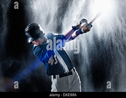 Young baseball player swinging bat dans la pluie Banque D'Images