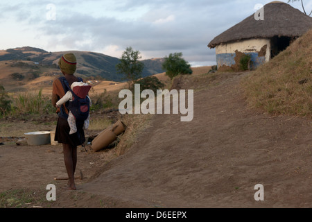 Une jeune fille africaine de marcher dans les collines près de sa maison, portant un bébé sur son dos Banque D'Images