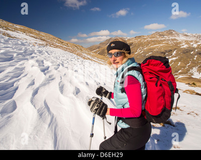 Une femme marche à travers l'affouillement sastrugi causés par le vent sur la neige au-dessus de Wrynose Pass, Lake District, UK. Banque D'Images