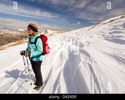 L'affouillement Sastrugi causés par le vent sur la neige au-dessus de Wrynose Pass dans le Lake District, UK avec une femme walker. Banque D'Images