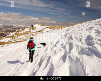 L'affouillement Sastrugi causés par le vent sur la neige au-dessus de Wrynose Pass dans le Lake District, UK avec une femme walker. Banque D'Images