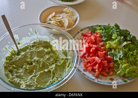 Bol plein de délicieux guacamole à côté d'une assiette de coupe la laitue et les tomates et un bol de croustilles de maïs Banque D'Images