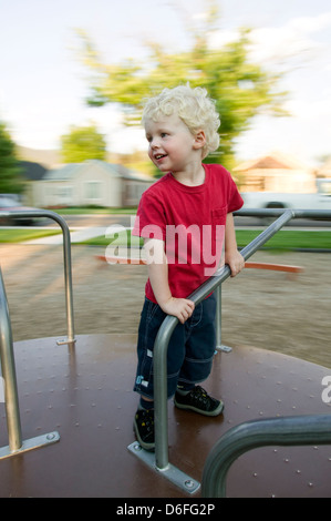 Garçon blond jouant sur un manège dans un parc sur l'aire de jeux. Banque D'Images