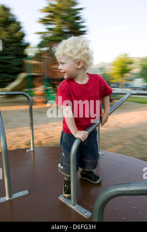 Garçon blond jouant sur un manège dans un parc sur l'aire de jeux. Banque D'Images