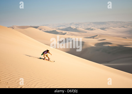 Sandboarding homme sur le désert qui entoure l'Oasis Huacachina, dans le sud-ouest du Pérou. Banque D'Images
