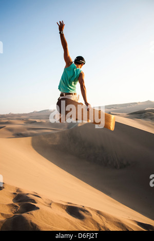 Sandboarder jumping and holding sa planche sur le désert qui entoure l'Oasis Huacachina, dans le sud-ouest du Pérou. Banque D'Images