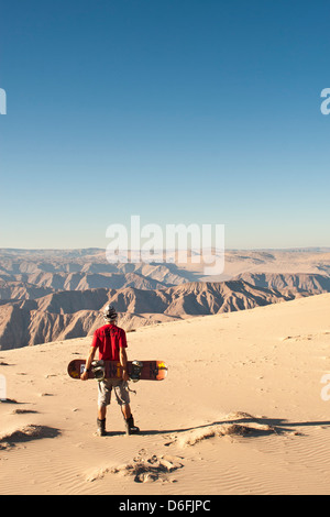 Jeune homme tenant un sandboard à la recherche de la vue depuis le Cerro Blanco, une dune de sable, sur le sommet d'une montagne avec 2078 mètres de haut. Banque D'Images