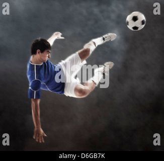 Soccer player kicking ball hispanique dans les airs Banque D'Images