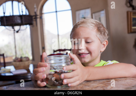 Boy putting économies dans un bocal en verre Banque D'Images