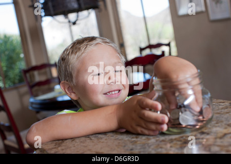 Boy putting économies dans un bocal en verre Banque D'Images