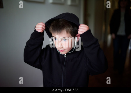 Jeune garçon met sa capuche sur son sweat à capuche tout en écoutant de la musique. Banque D'Images