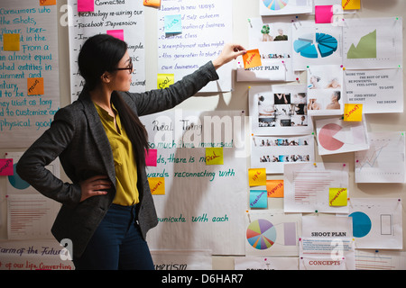 Femme avec des notes adhésives et des papiers sur le mur Banque D'Images