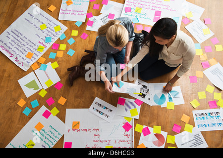 Collègues assis sur le plancher avec des papiers et notes adhésives Banque D'Images