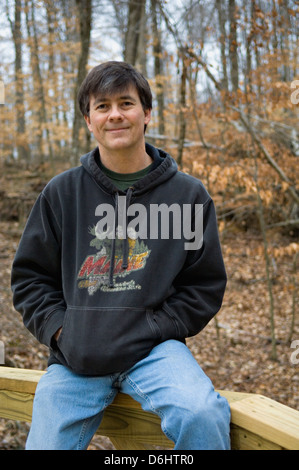 Middle aged Man Sitting on Rail de Bridge in forest Banque D'Images