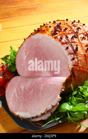 Jambon cuit au four avec des clous de girofle et les tomates cerises et couteau et fourchette sur un plateau d'argent sur un fond de bois Banque D'Images