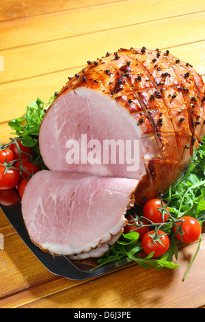 Jambon cuit au four avec des clous de girofle et les tomates cerises et couteau et fourchette sur un plateau d'argent sur un fond de bois Banque D'Images