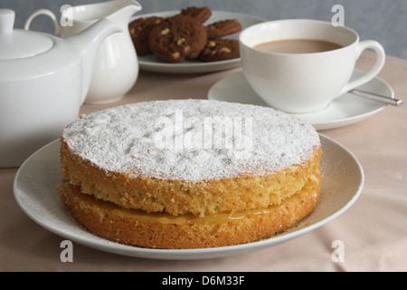 Un gâteau éponge victoria citron servi avec une tasse de thé et des biscuits. Banque D'Images