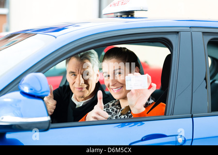 Auto-école - Jeune femme diriger une voiture, peut-être qu'elle a un examen de conduite, elle tenant fièrement son permis de conduire Banque D'Images