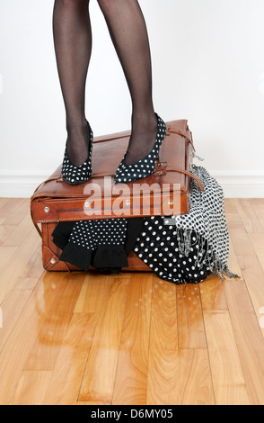 Femme de hautes chaussures de talon debout sur le cuir valise trop plein avec la mode des vêtements. Banque D'Images