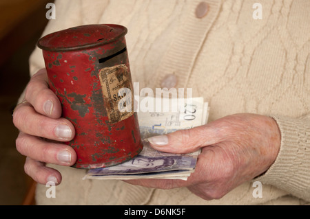 Femme âgée maintenant de 20 livres notes sous l'étain d'épargne battues Banque D'Images