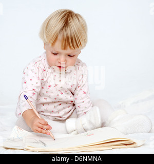 Petite fille assise sur le lit avec un crayon dessin Banque D'Images