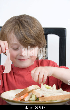 Smiling Young boy picks outre son sandwich salade et sort le jambon délicieux aliments sains de remplissage : studio portrait Banque D'Images