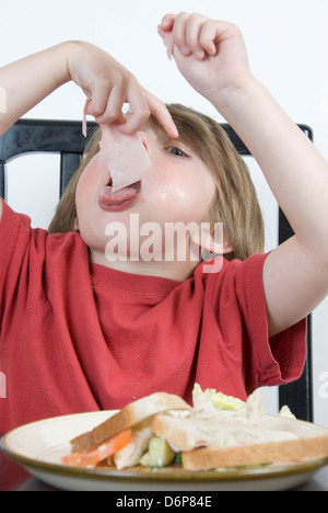 Jeune garçon mangeant une tranche de jambon a sélectionné à partir du milieu de son sandwich salade : alimentation saine studio portrait Banque D'Images