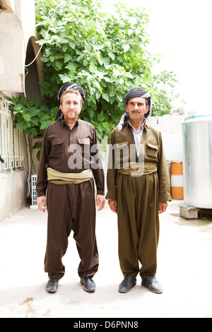 Les deux hommes en vêtements traditionnels et couvre-chef, l'un avec une arme à la ceinture, debout dans l'avant-cour de leur maison. Banque D'Images