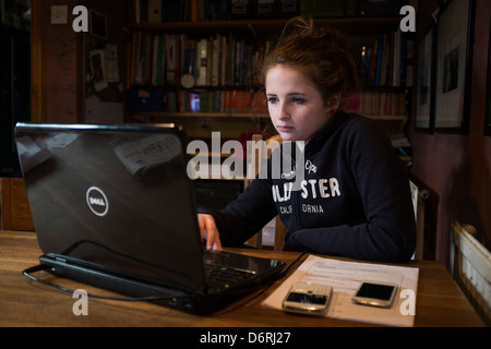 Une jeune fille de quatorze ans à l'aide de son ordinateur portable et deux téléphones mobiles à la maison - travail, social networking, uk Banque D'Images