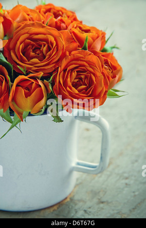 Mug blanc avec un bouquet de roses orange sur fond de bois vintage vert Banque D'Images