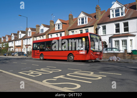 Bus se déplaçant sur une rue bordée de maisons du 19e siècle à Twickenham, l'Angleterre, avec l'arrêt de bus le marquage routier en premier plan Banque D'Images