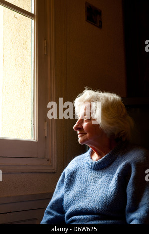 Portrait de vieille femme à la maison, souriant et regardant la fenêtre. Banque D'Images