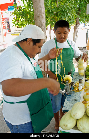 Fils regardant son père utiliser une machine à main peeling fruit à un stand de fruits au centre-ville, Cancun, Quintana Roo, Mexique Banque D'Images