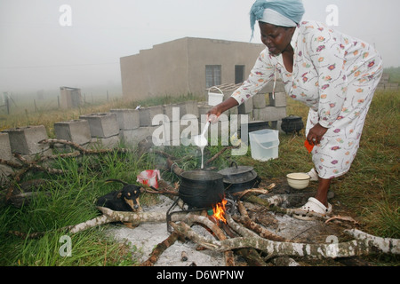 Une femme africaine cuisiniers à l'extérieur sur un feu de bois comme la brume en rouleaux Banque D'Images