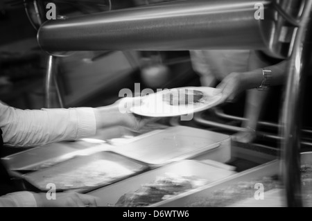 Image floue des traiteurs servant de la nourriture chaude dans une cantine. Banque D'Images