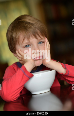 Un garçonnet de cinq ans avec les cheveux bruns et les yeux bleus de manger un bol de céréales pour son petit-déjeuner. Banque D'Images