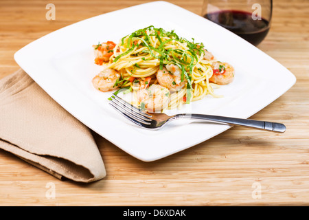 Photo horizontale gros plan d'un plat de pâtes avec l'accent sur de grosses crevettes en fourche en acier inoxydable, basilic, serviette en tissu et le vin rouge Banque D'Images