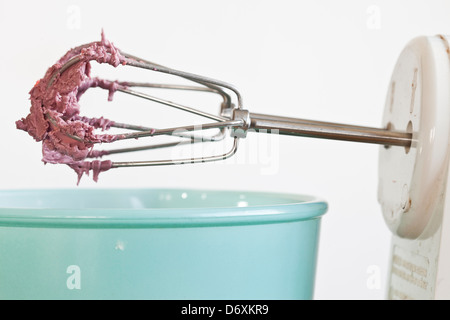 Mixeur électrique avec glaçage rouge/rosé sur les fouets avec un bol bleu, Banque D'Images