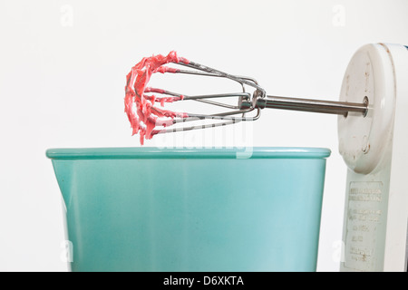 Mixeur électrique avec glaçage rouge/rosé sur les fouets avec un bol bleu, Banque D'Images