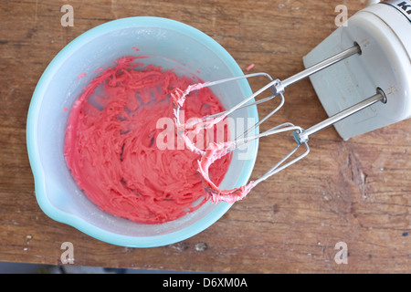 Mixeur électrique avec glaçage rouge/rosé sur les fouets avec un bol bleu, Banque D'Images