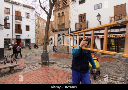 Un homme avec une échelle de géant à travers la place du marché de la Plaza Larga, dans le centre de l'Albaicin, Grenade Banque D'Images