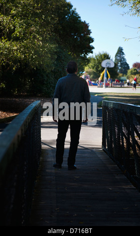 Vue arrière d'un homme dans un parc à marcher en direction d'une aire de jeux pour enfants. Banque D'Images