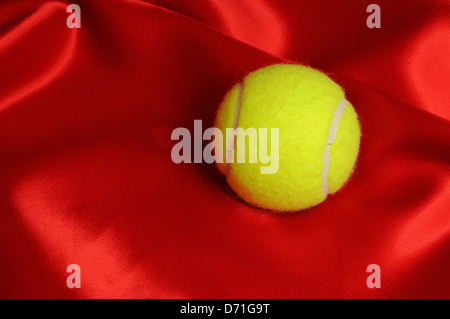 Balle de tennis sur fond de satin rouge. Banque D'Images