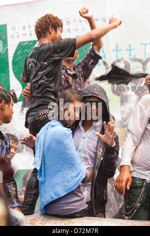 Les jeunes hommes grimpent sur les véhicules en mouvement à la danse et se font avoir comme ils passent par les plates-formes de l'eau au cours de la célébration. Thingyan Banque D'Images