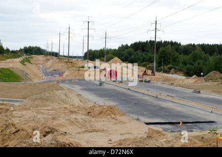 Voitures go round rond-point et nouveau chantier de construction routière, des poteaux électriques haute tension et fils. Banque D'Images