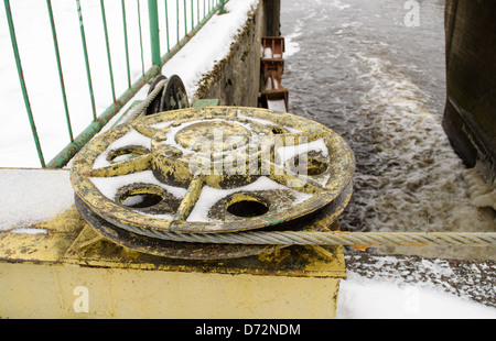 Vintage mécanisme barrage vis avec câble d'acier tendu d'acier recouvert de neige et le débit d'eau en hiver. Banque D'Images